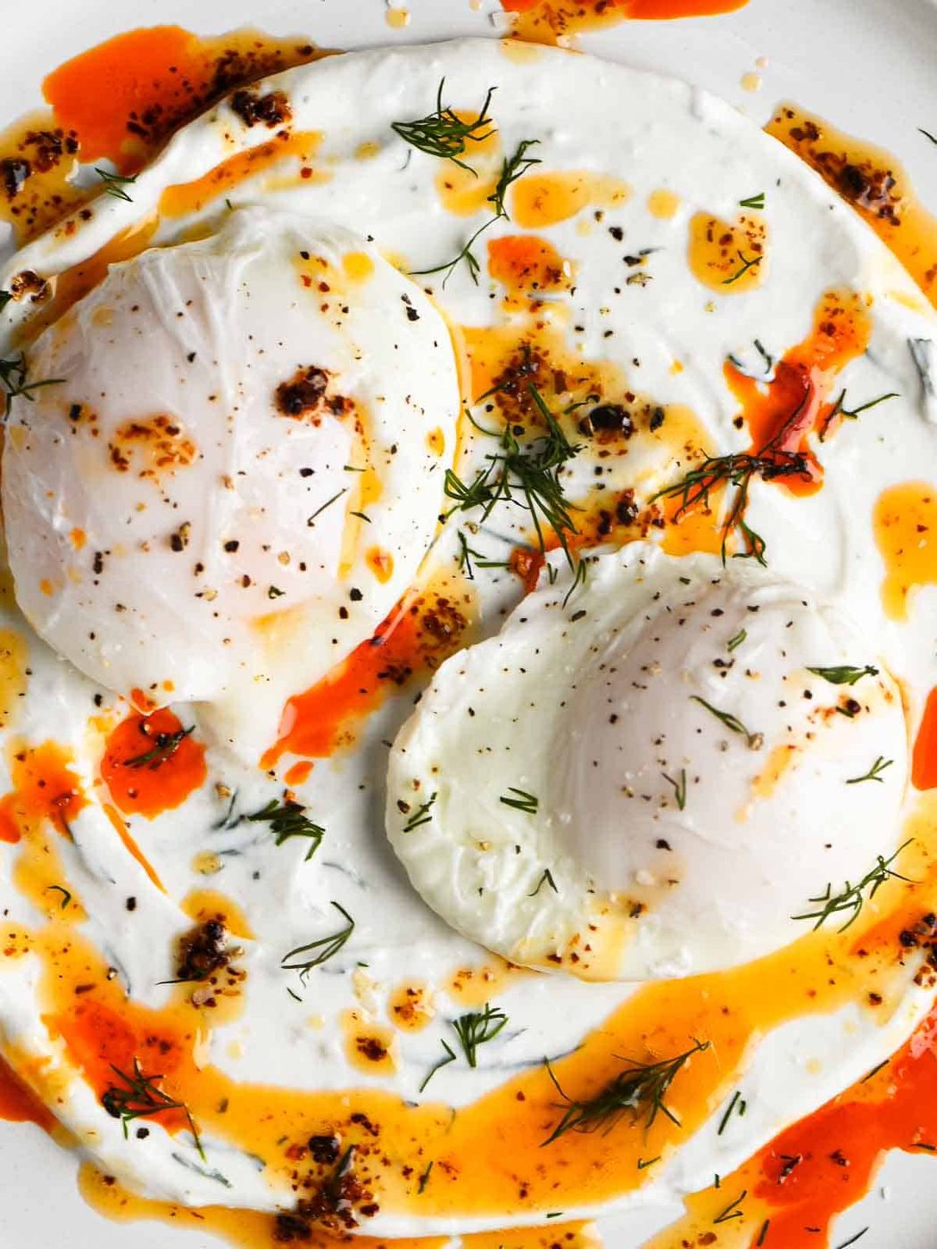Overhead of two poached eggs on a white dish with yogurt and chili butter.