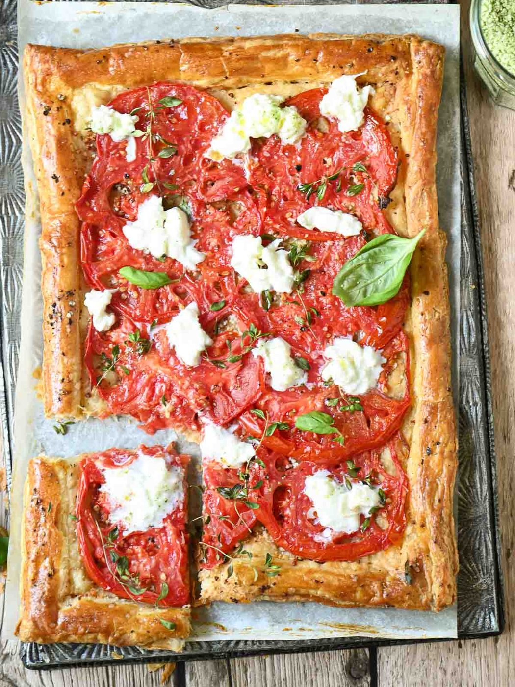 An overhead shot of a tomato tart with stracciatella on top of a metal baking tray.