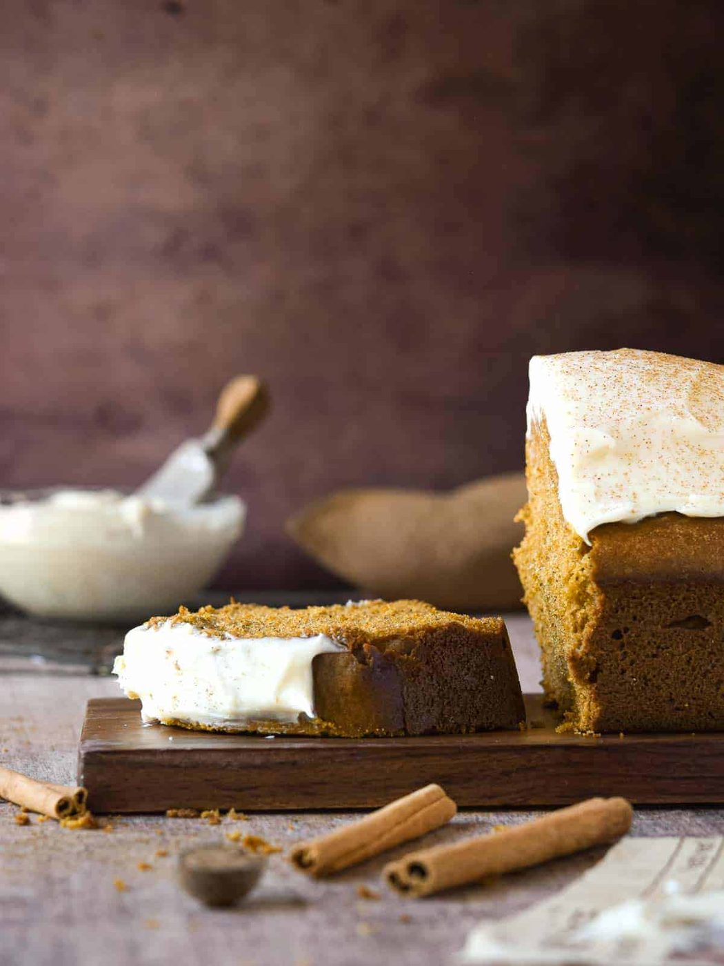 Side view of pumpkin bread cut, with one slice laying flat with frosting in the background.