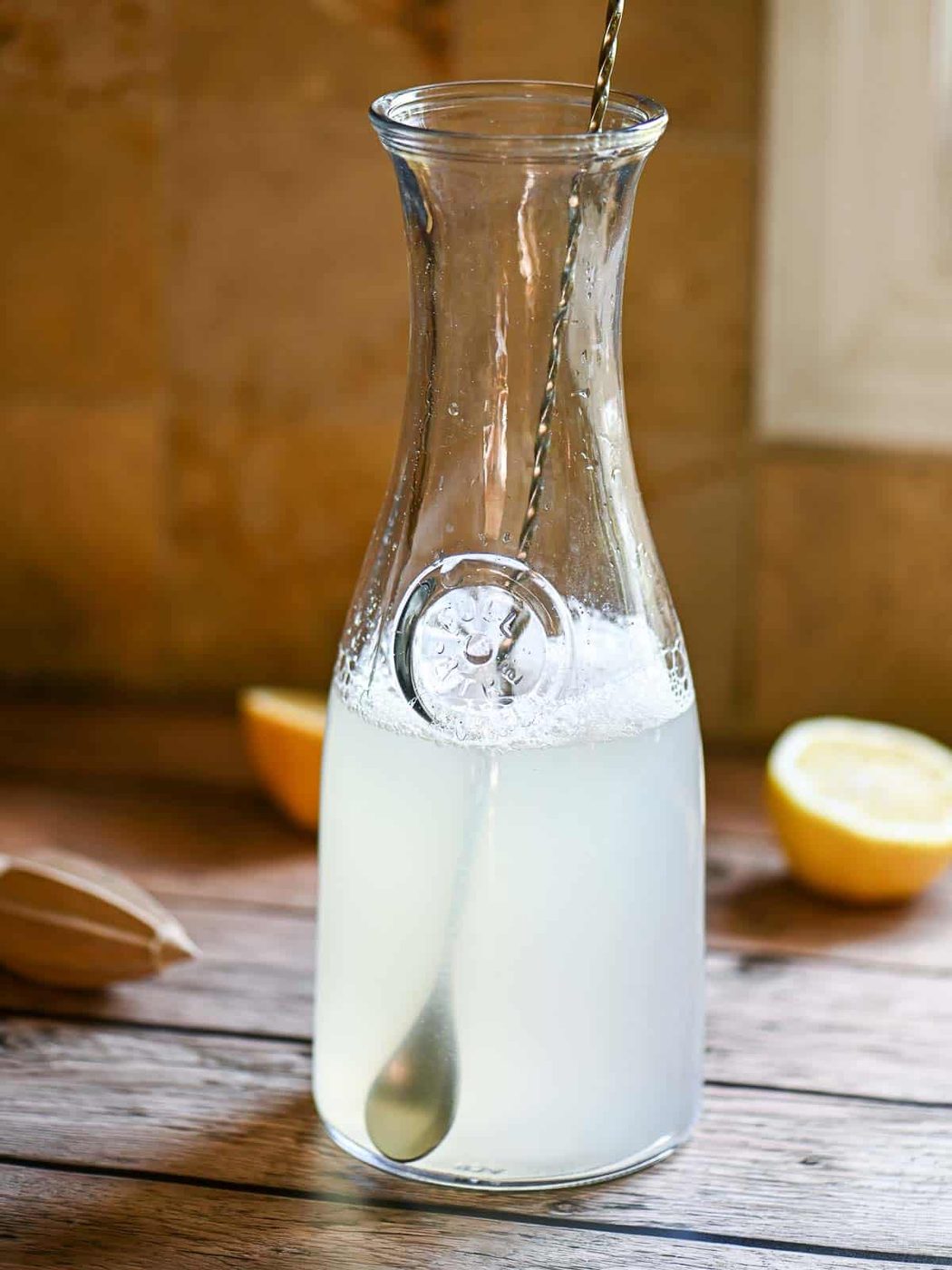 A pitcher with a spoon and lemon slices on a wooden table.