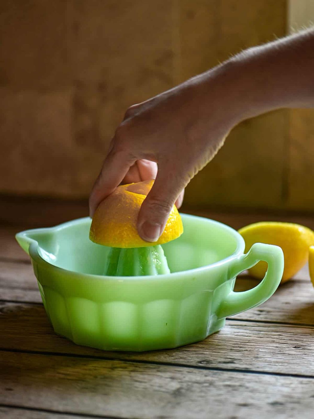 A hand squeezing a lemon over a green juicer.