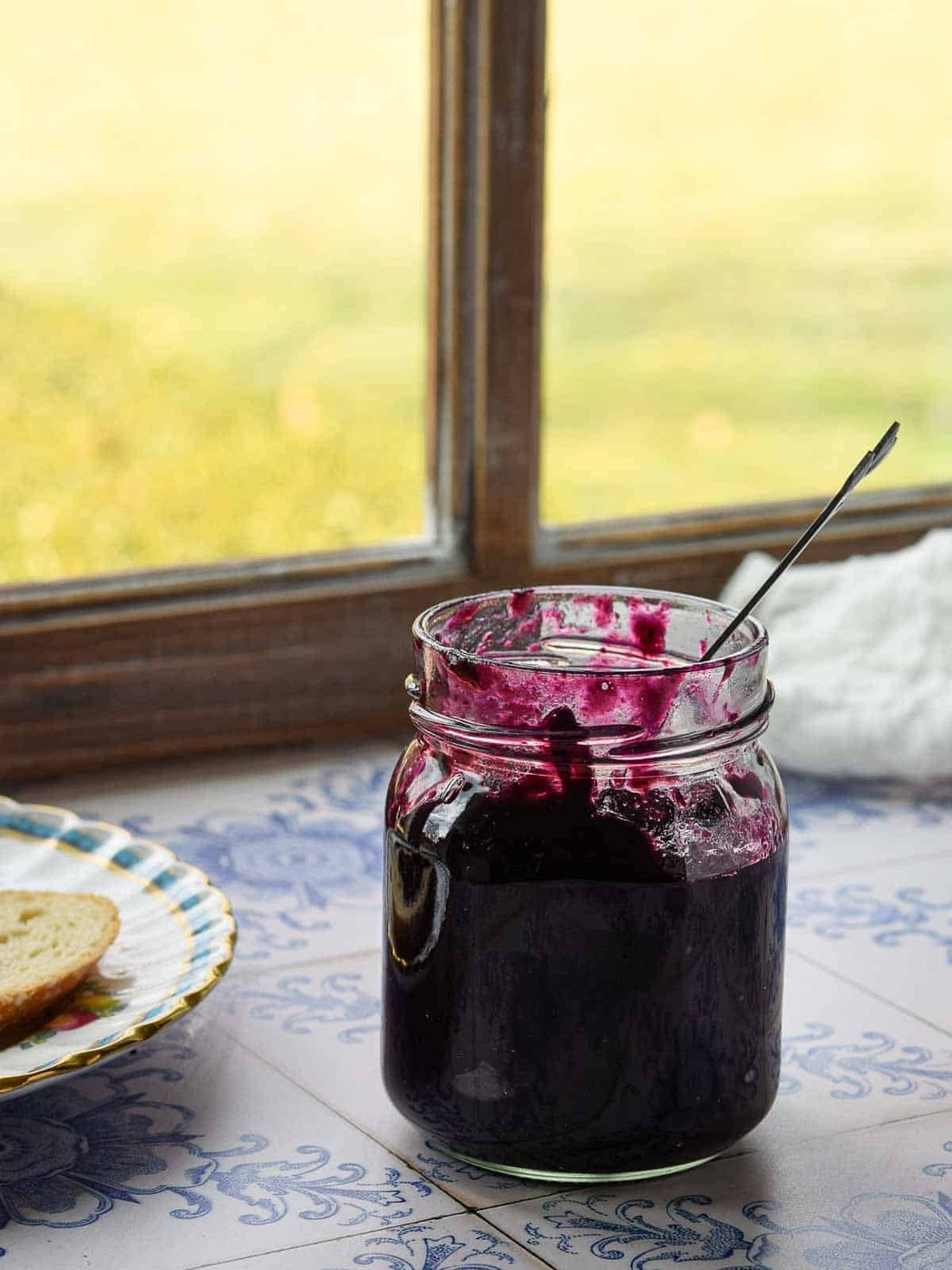 Blueberry earl grey jam in a glass jar by the window with light coming in.