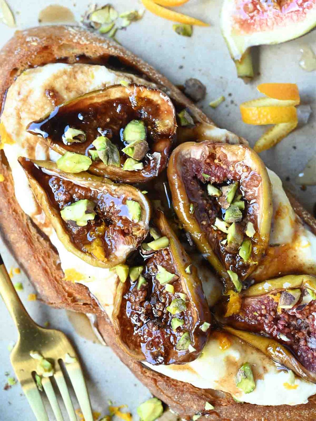 Overhead view of figs on toast with crushed pistachios and orange zest on top.