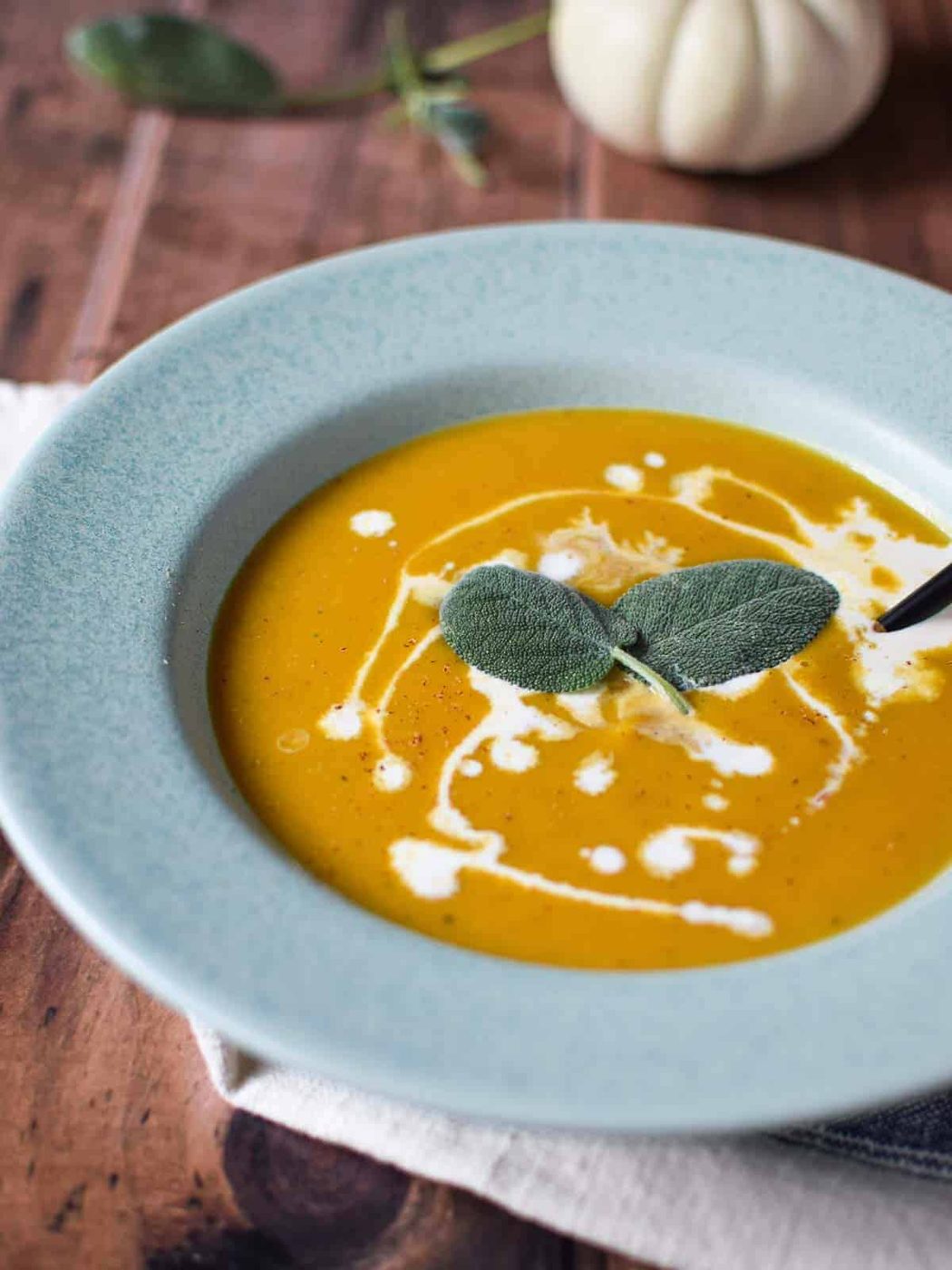 Squash soup with sage and cream drizzles on top in a blue bowl.