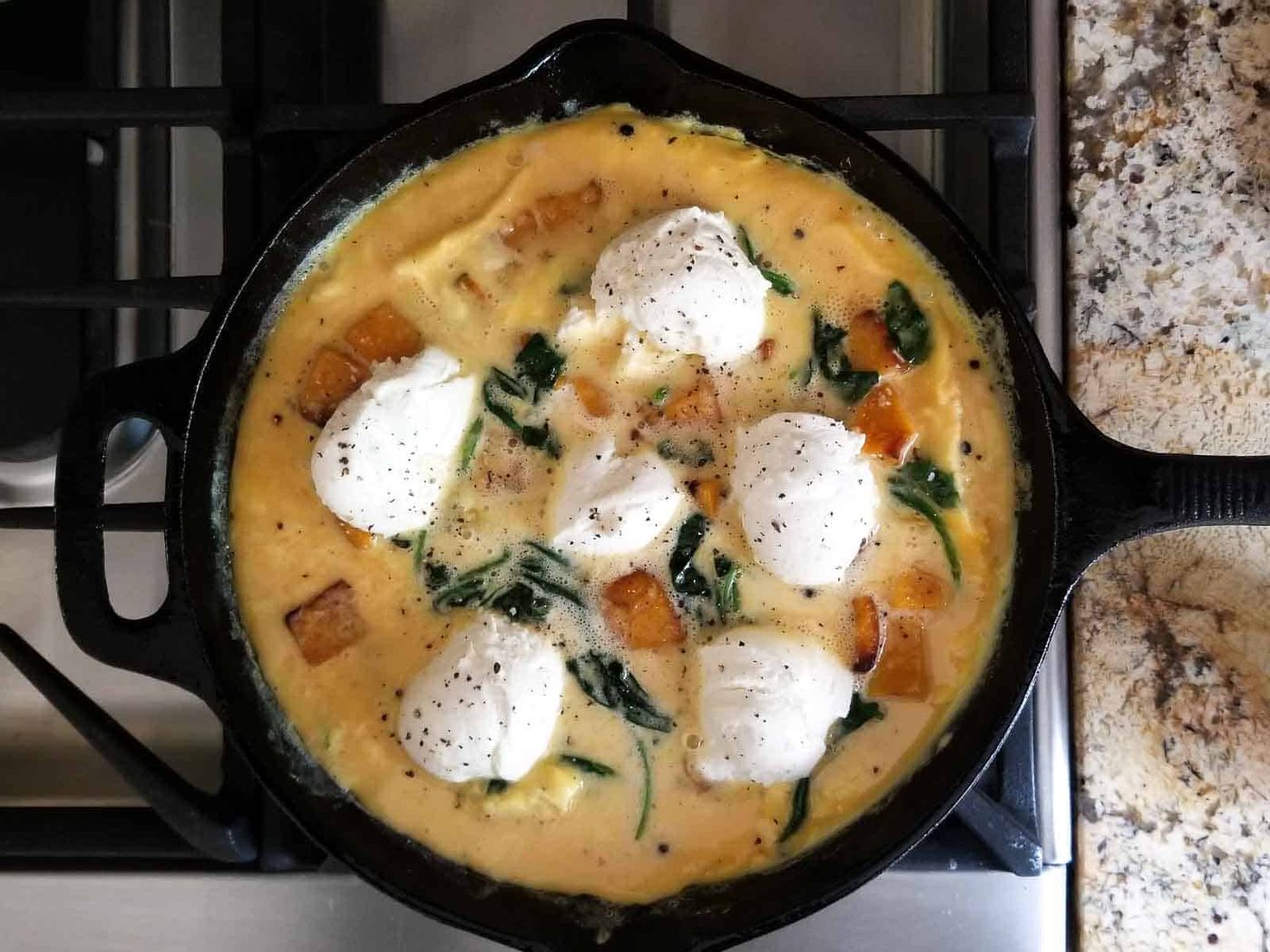 Process shot of half cooked frittata topped with ricotta about to be finished in the oven.