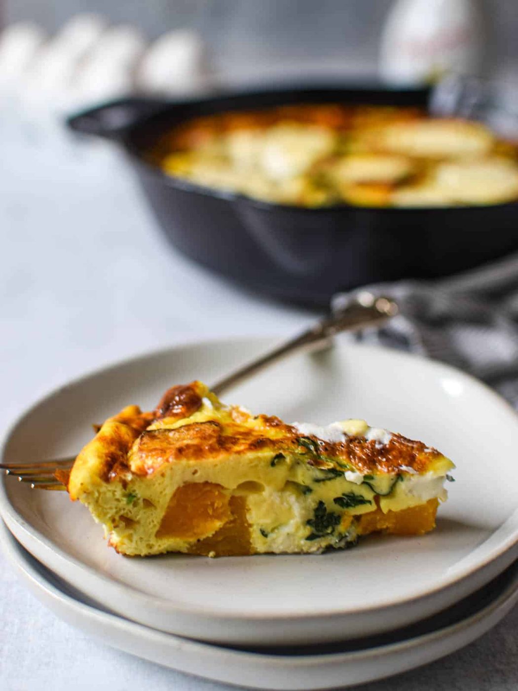 Close up slice of butternut squash frittata on white plate with remaining frittata in the background.
