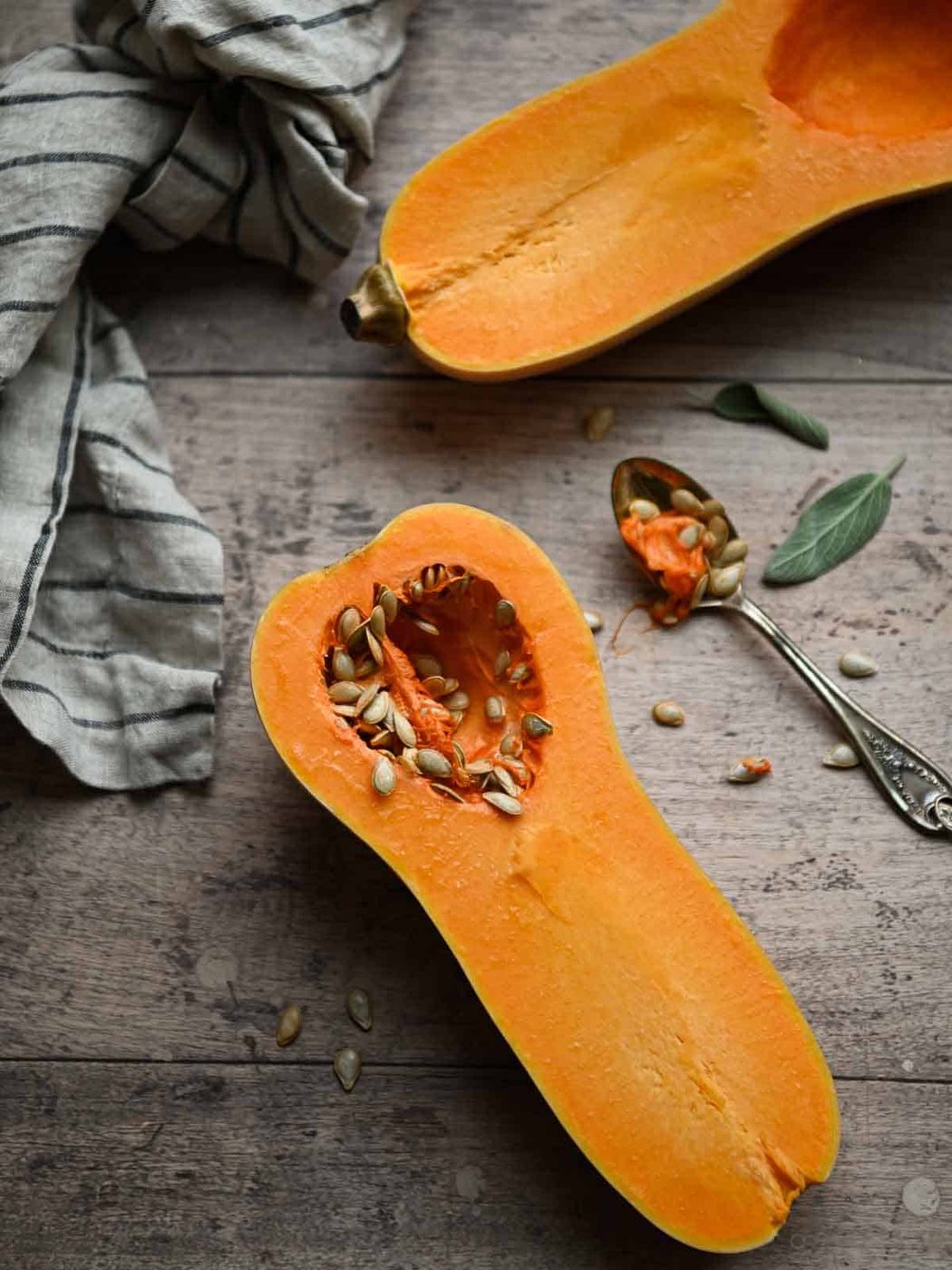 Overhead of butternut squash sliced in half and the seeds being scooped out.