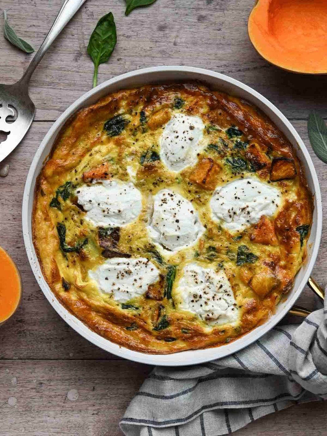 Overhead of a cooked frittata in a white skillet on a wood surface.