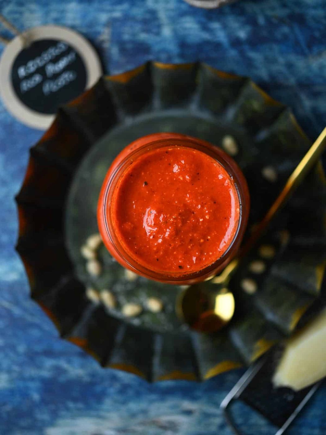 Overhead of red pepper pesto in a clear jar on top on a round grey plate.