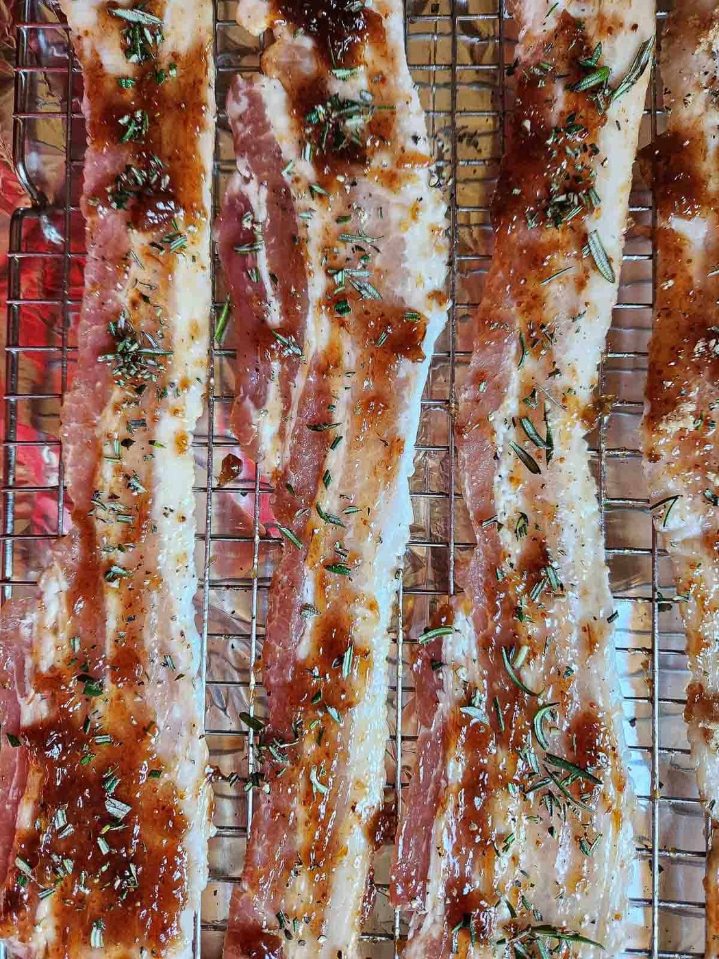 Raw bacon on a baking sheet with fig jam and rosemary on top.
