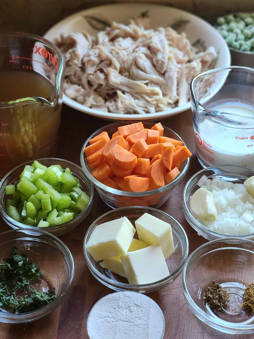 Ingredients for chicken pot pie filling in little bowls on a wood surface.