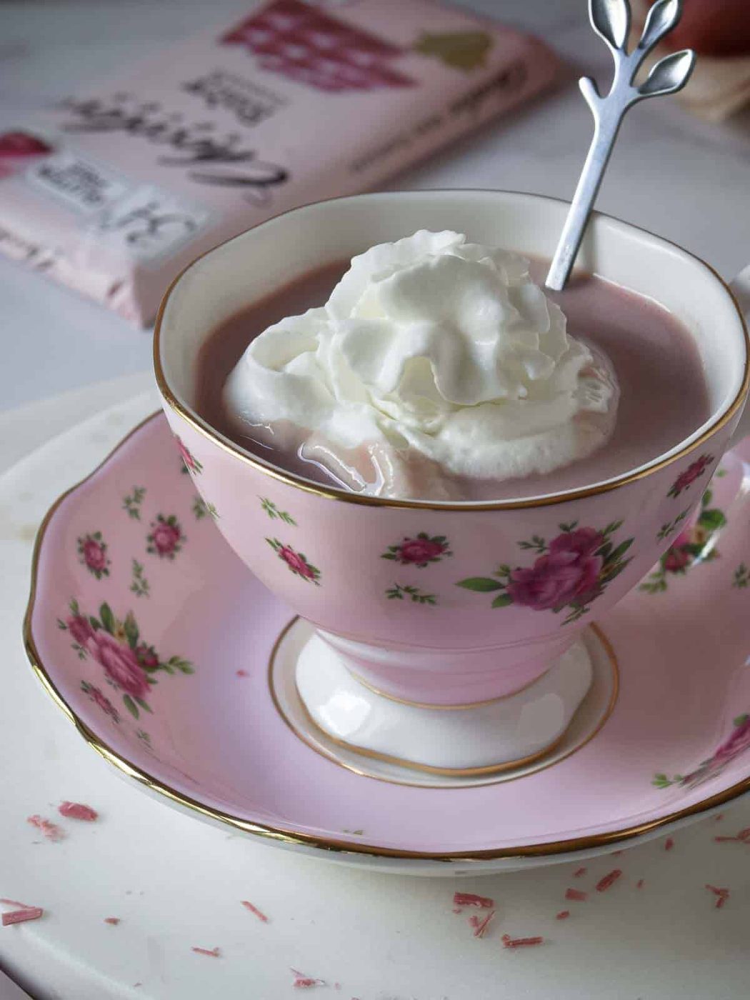 Angled view of ruby hot chocolate with whipped cream in a pink floral cup.