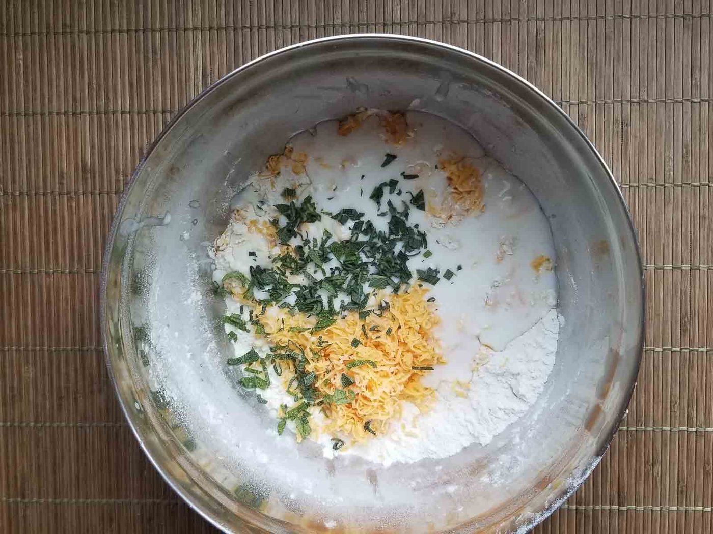 Ingredients for cheddar sage biscuits mixed in a bowl.