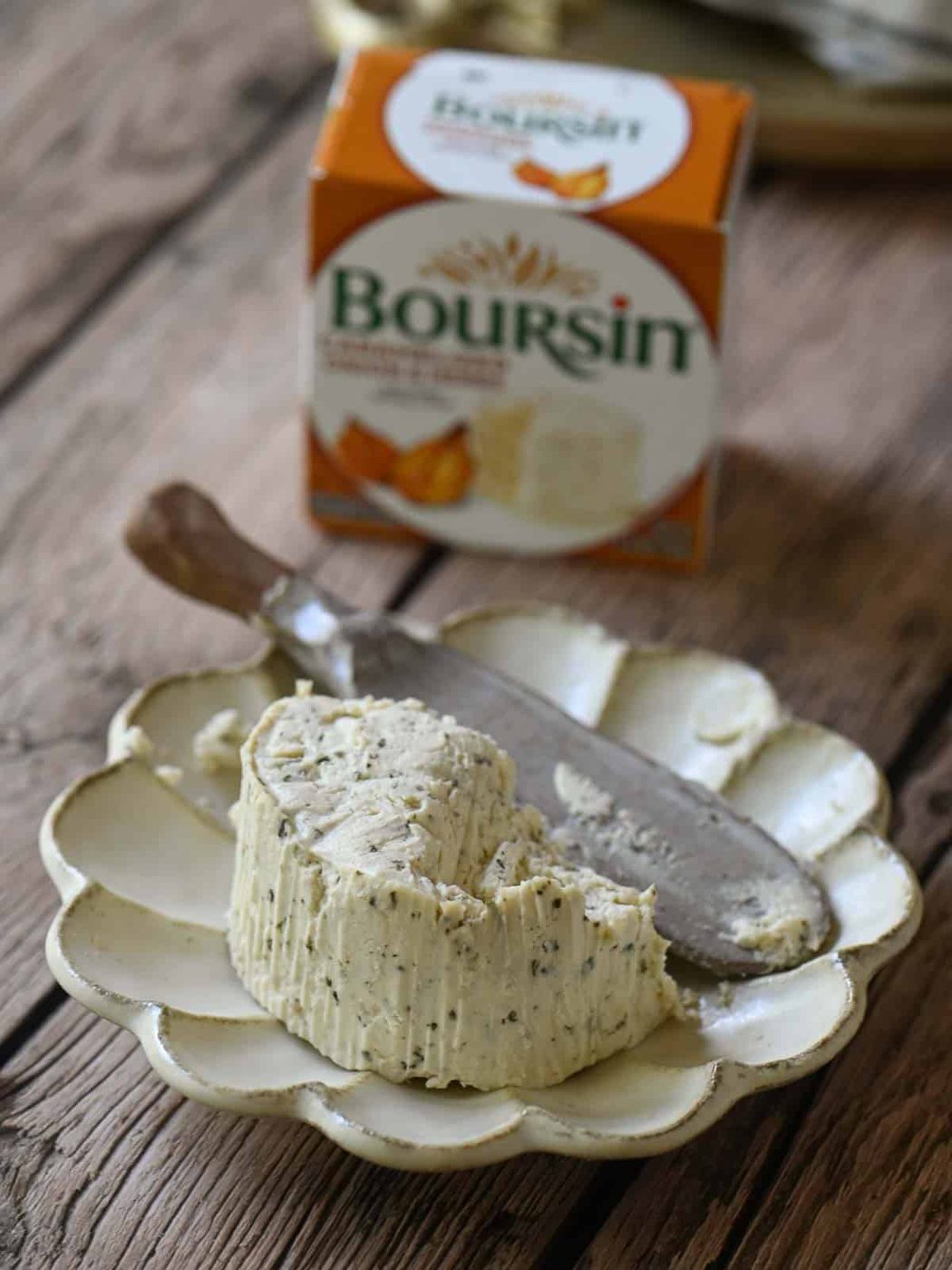 A close-up of Boursin cheese on a scalloped plate with a spreader.