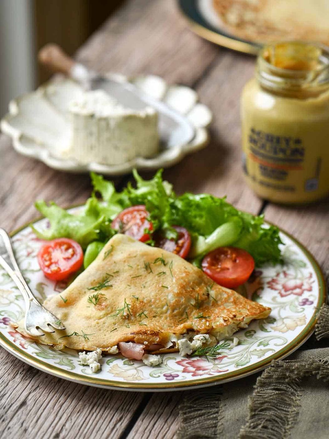 Savory crepes on a plate with a tomato and lettuce salad in the back.