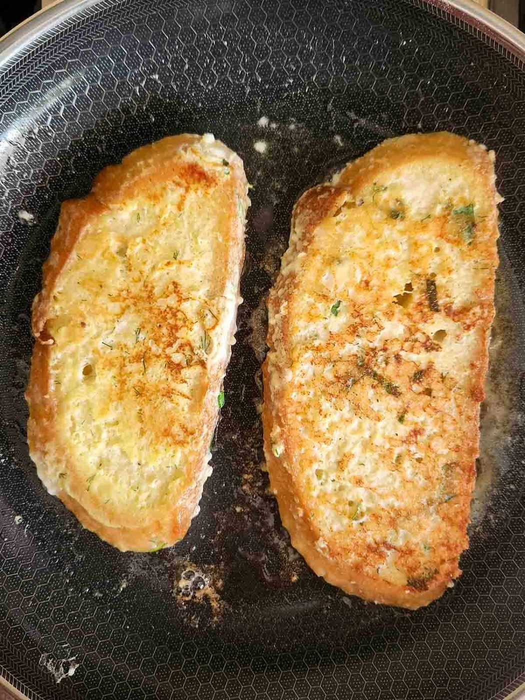 Two slices of French toast in a pan being showing the browned cooked side.