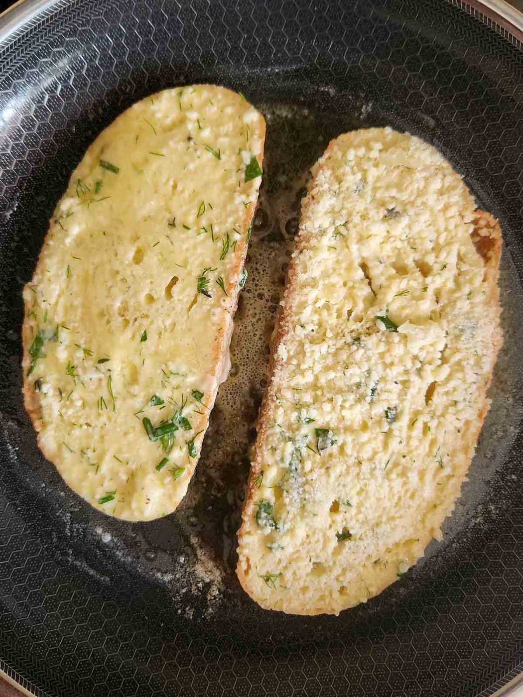 Two slices of French toast in a pan being sauteed.