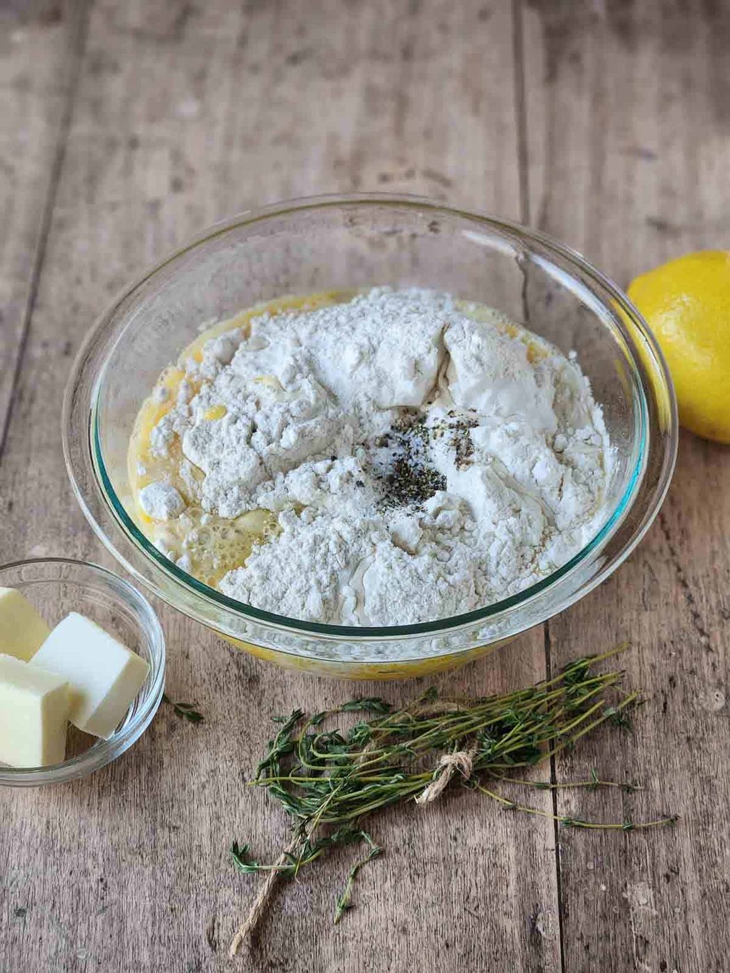 Batter for lemon-thyme popovers in a clear bowl with thyme and lemon on the side.
