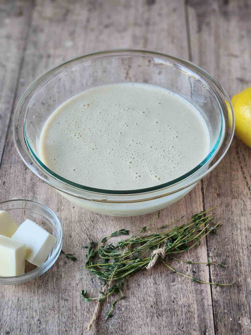 Batter for lemon thyme popovers in a clear bowl on a wood surface.