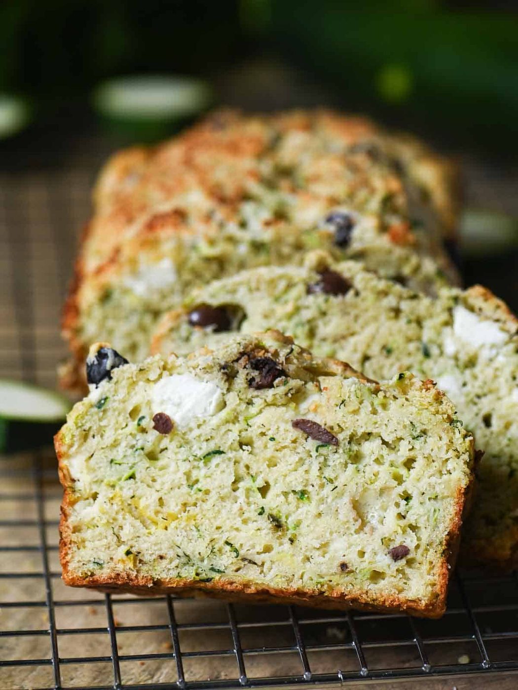 Savory zucchini bread slices leaning against each other on a metal rack.