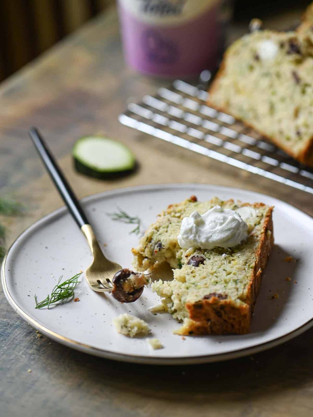 A serving of zucchini bread on a beige plate with yogurt and a fork to the left.