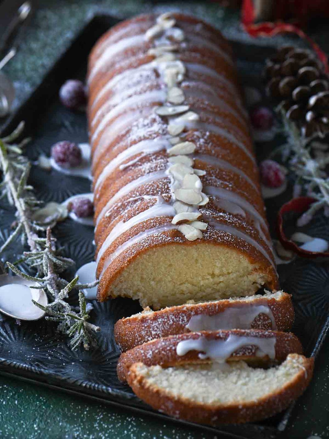 Angled view on an almond cake with icing on top and sugared cranberries.