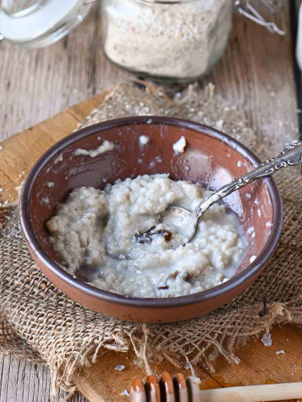 Half eaten bowl of oatmeal in a brown bowl with a spoon the right.