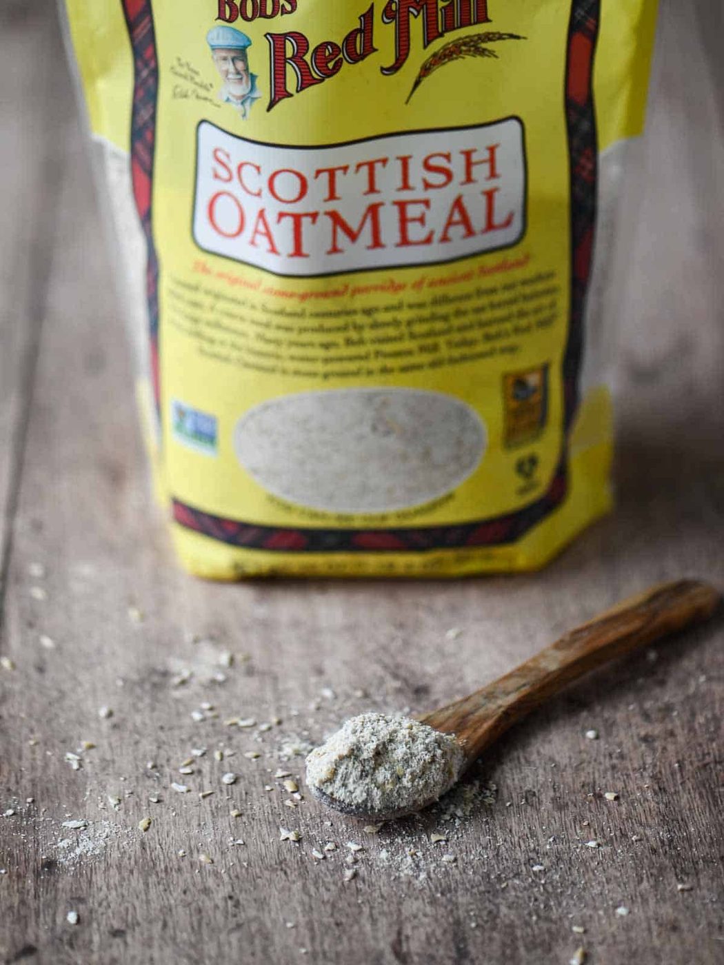 Raw Scottish oats on a wooden spoon, with a bag of Scottish oats in the background.