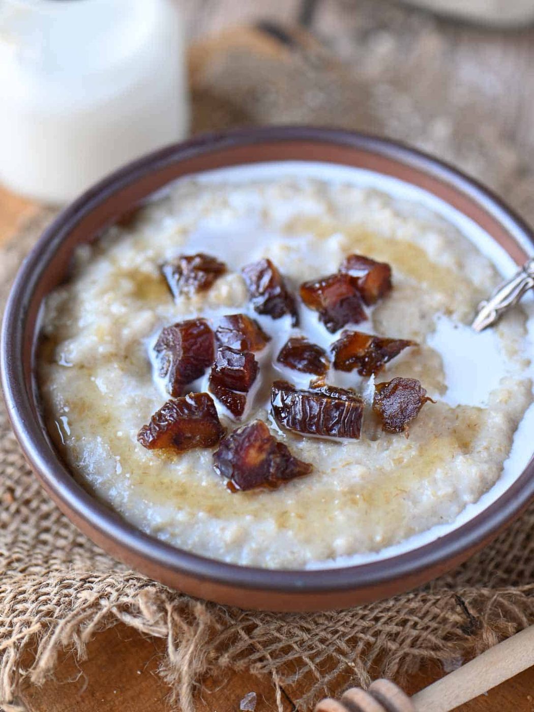 Angled view of oatmeal in a brown bowl with dates on top.