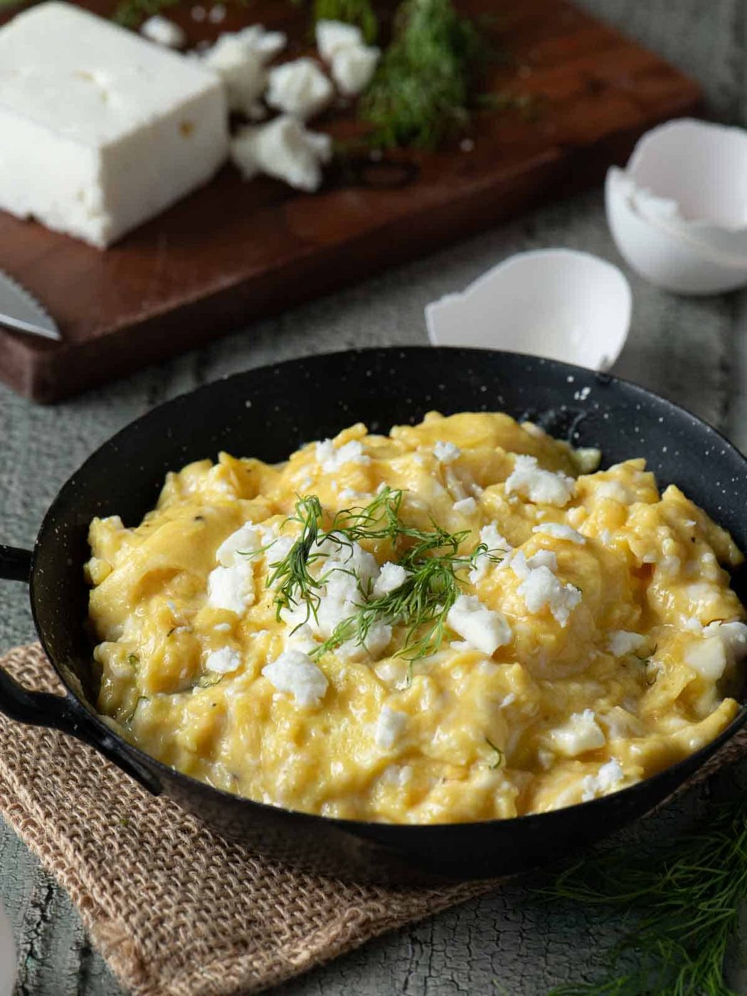 Angled view of scrambled eggs in a skillet with feta on top.