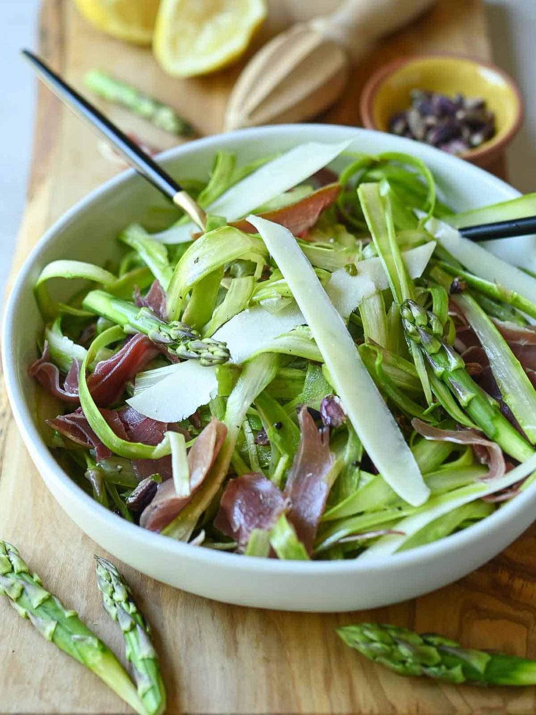 Angled view of shaved asparagus salad on a wood board with utensils in it.