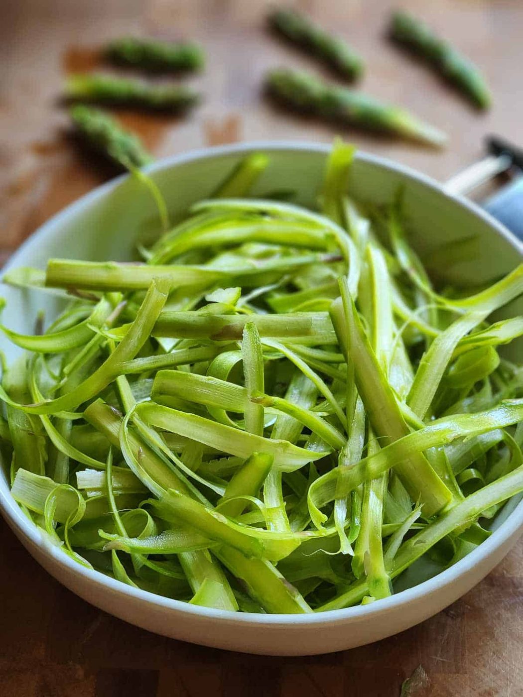 Shaved asparagus in a white bowl on a cutting board.