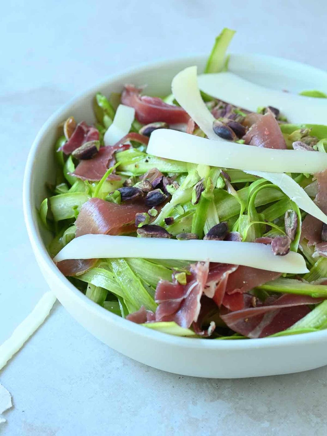 Asparagus salad in a white bowl with toppings.