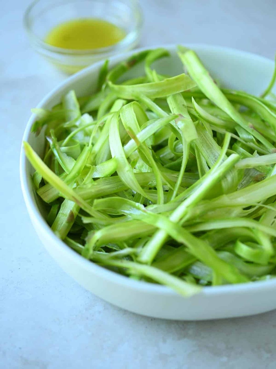 Raw shaved asparagus in a white bowl.