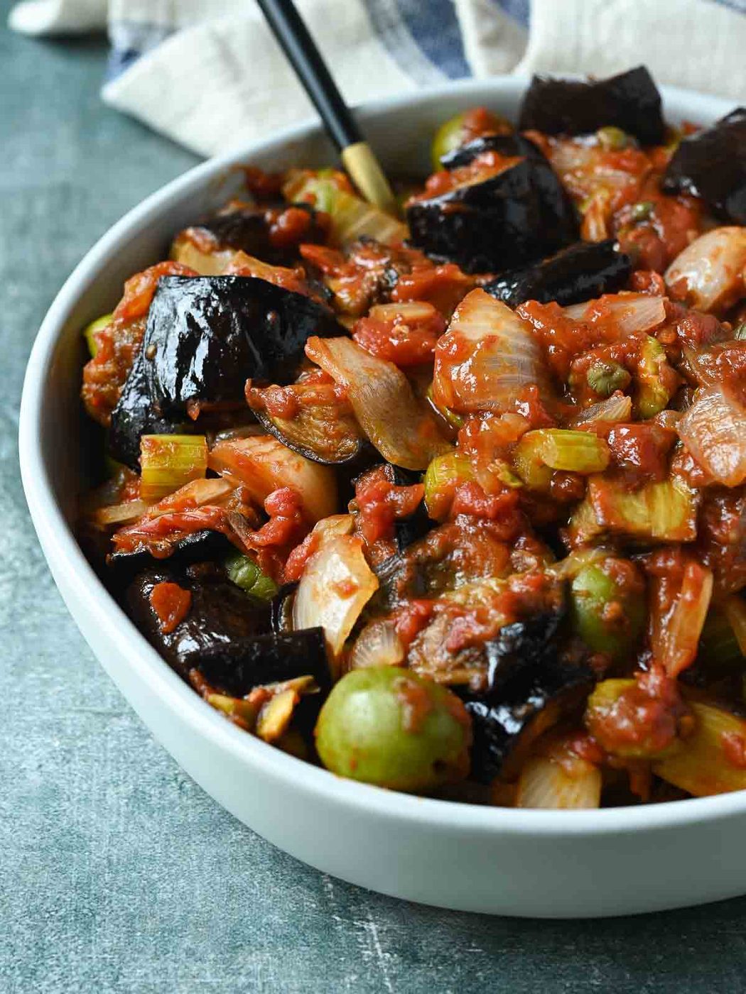 Eggplant caponata in a white bowl on a blue surface.