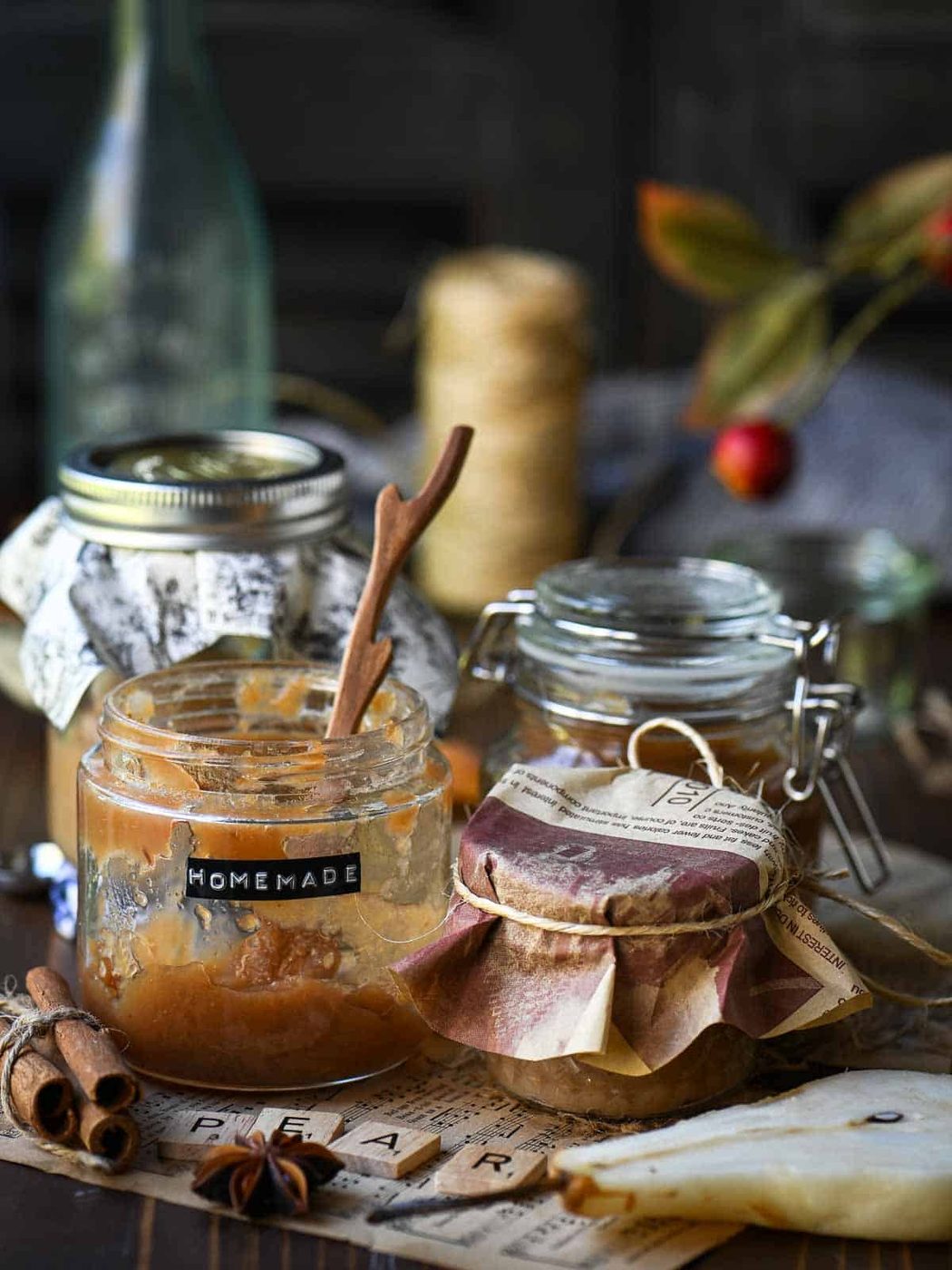 Four jars of pear butter in various sizes with spices and a sliced pear around it.