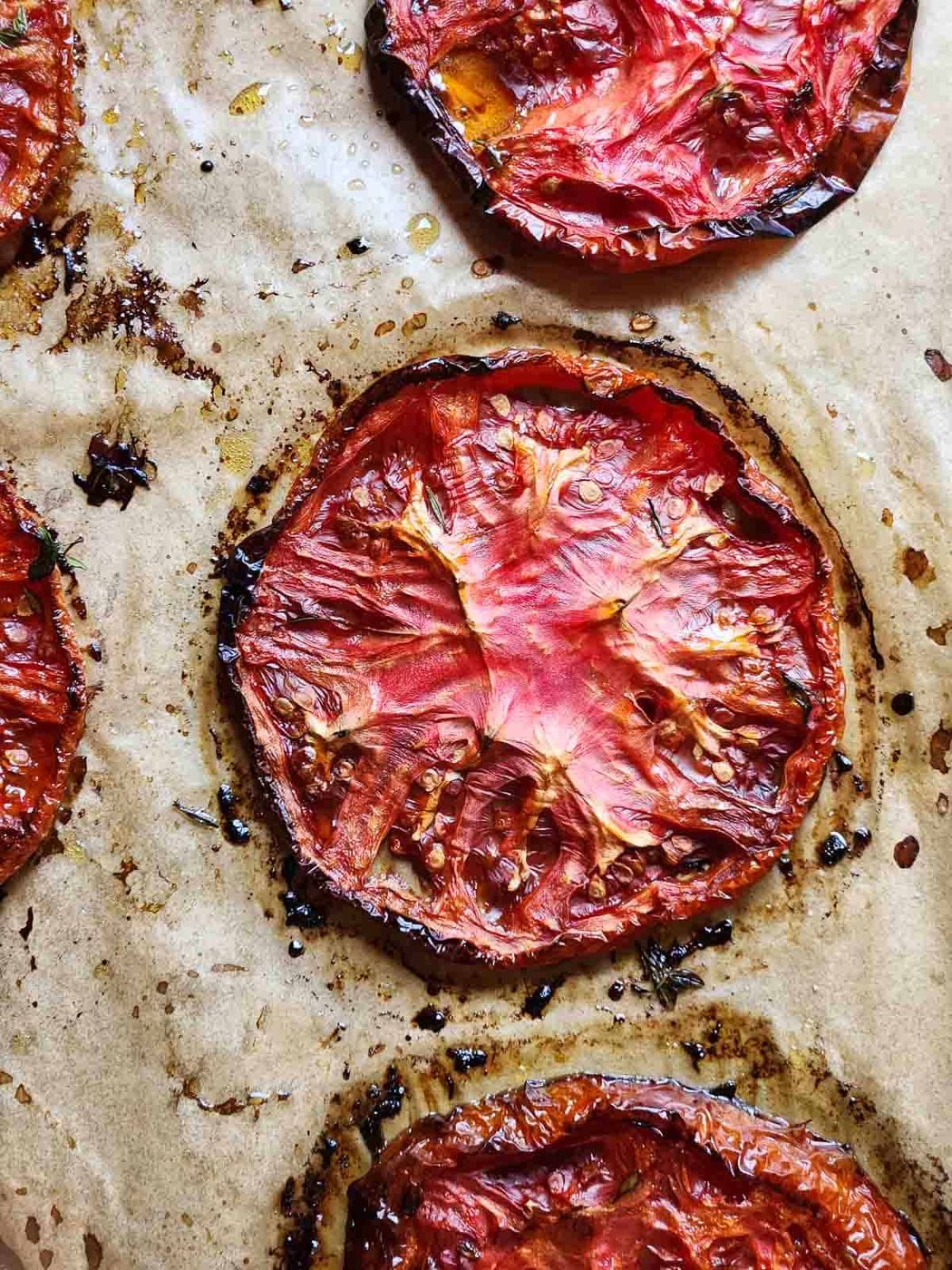 Overhead of roasted beefsteak tomatoes on brown parchment paper.
