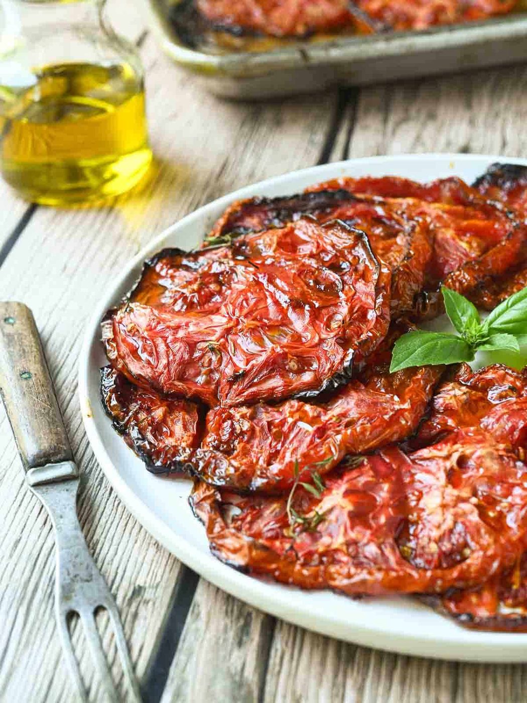 Roasted red tomatoes on a white plate with a fork next to it.