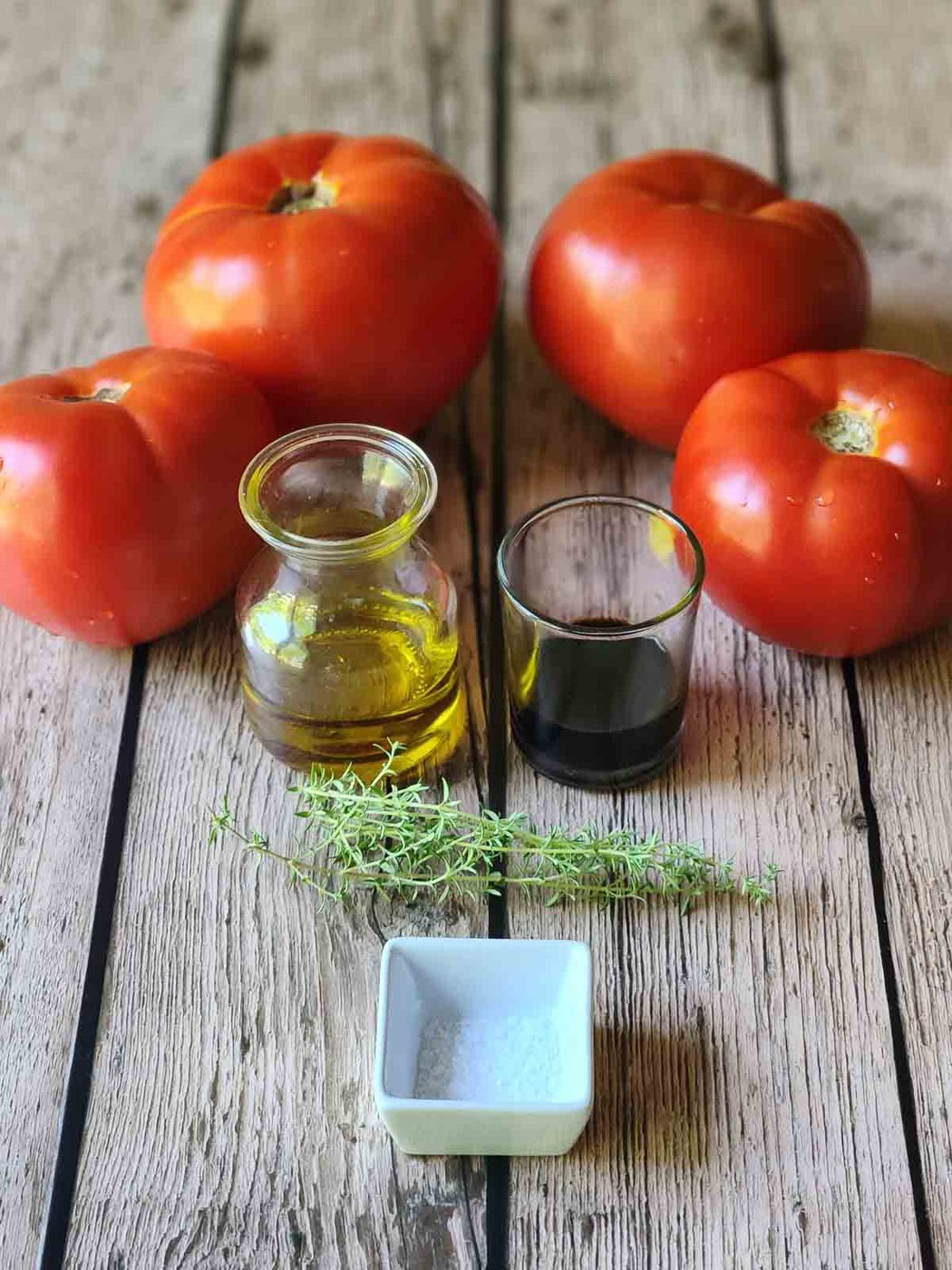 Ingredients for roasted tomatoes on a wooden surface.