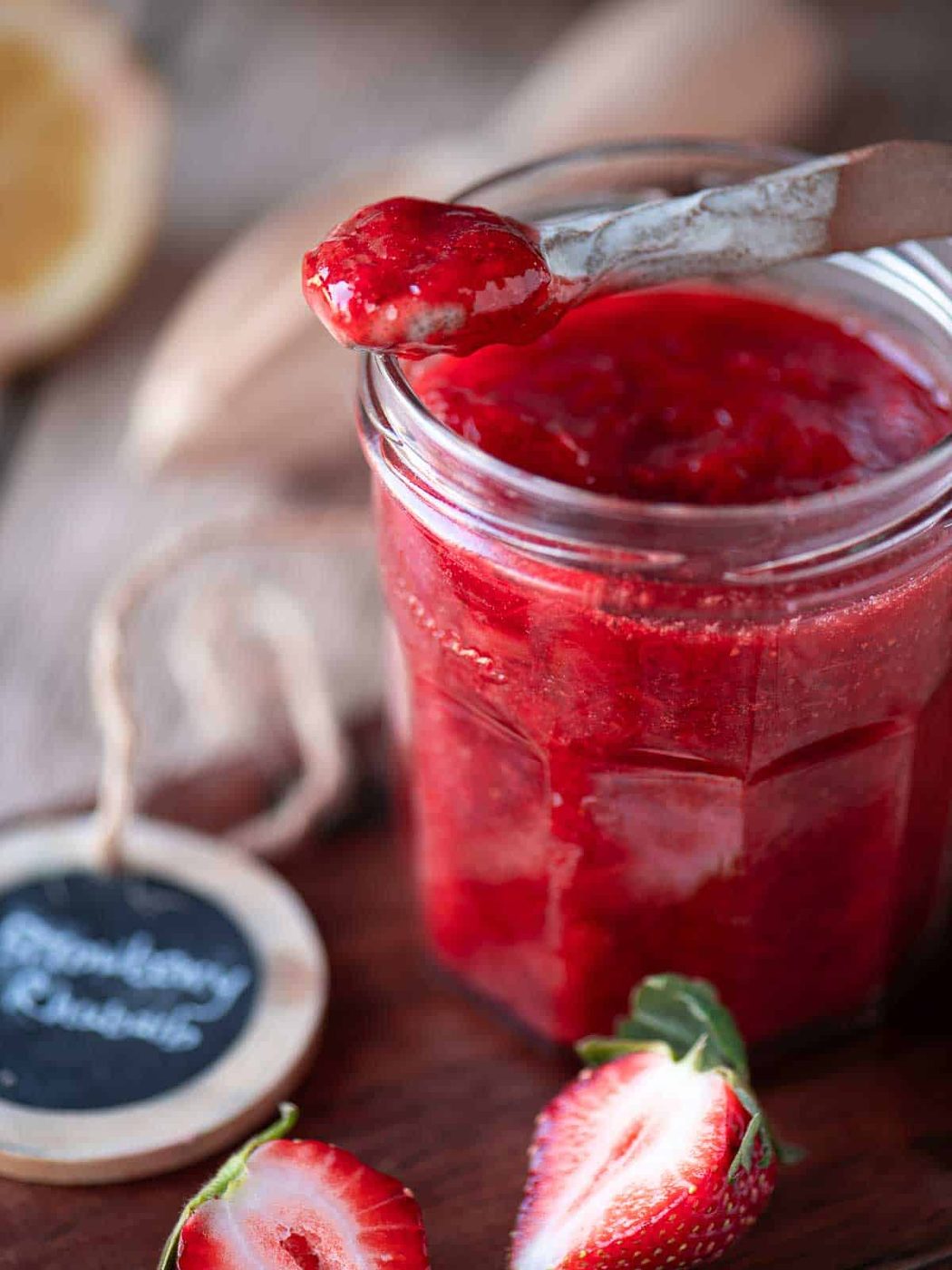 Close up of a spoon dipped into strawberry jam in a clear jar.