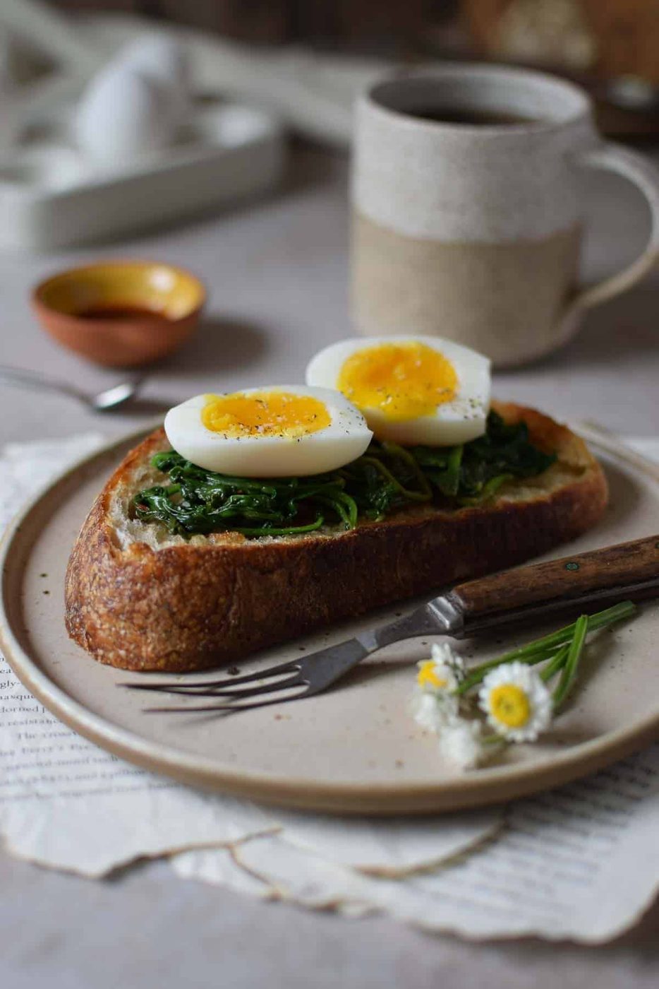 Jammy eggs on toast with spinach with coffee in the background.