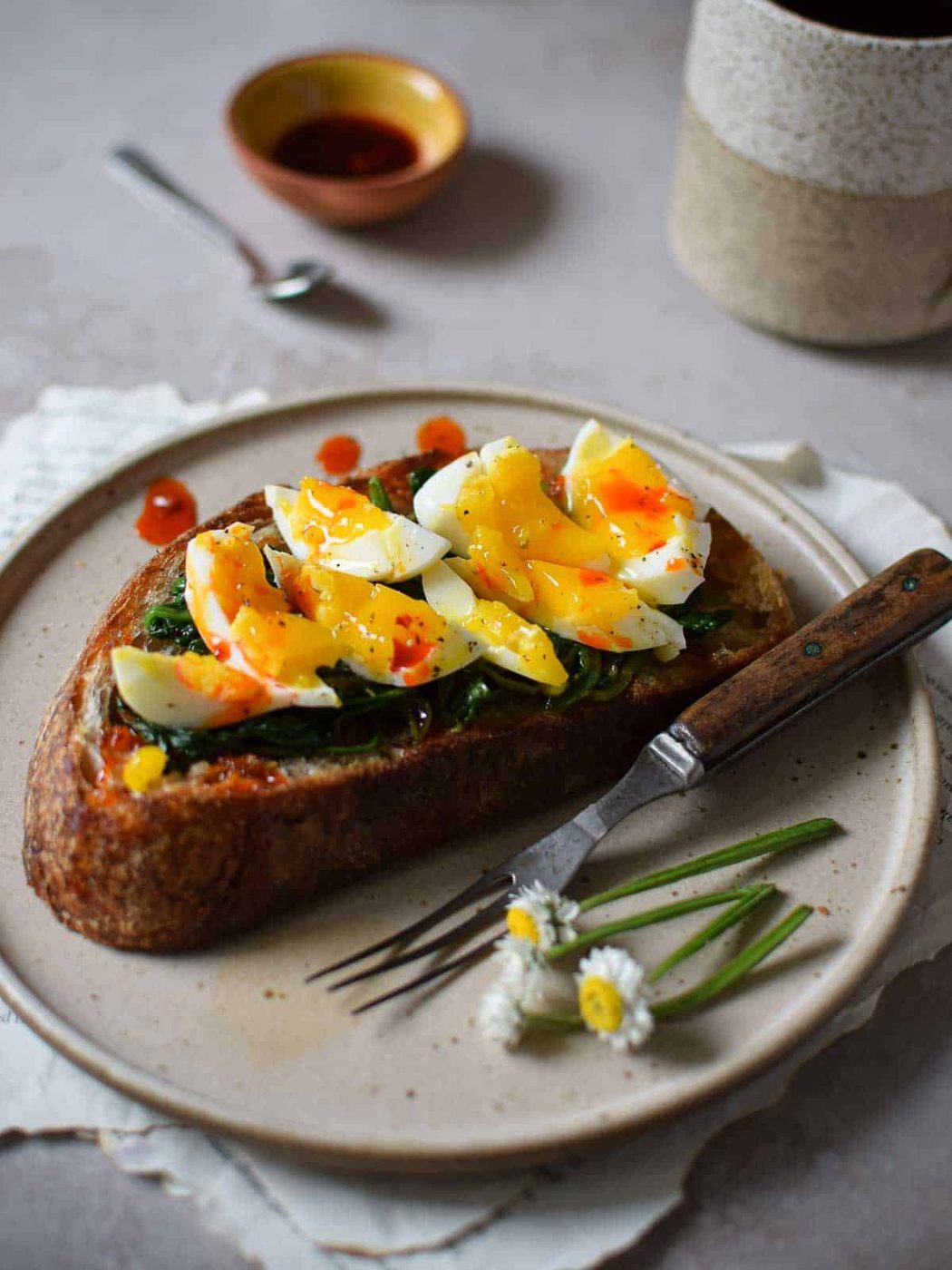 Angled view of smashed eggs on toast with chili oil drizzled on it on a brown plate.