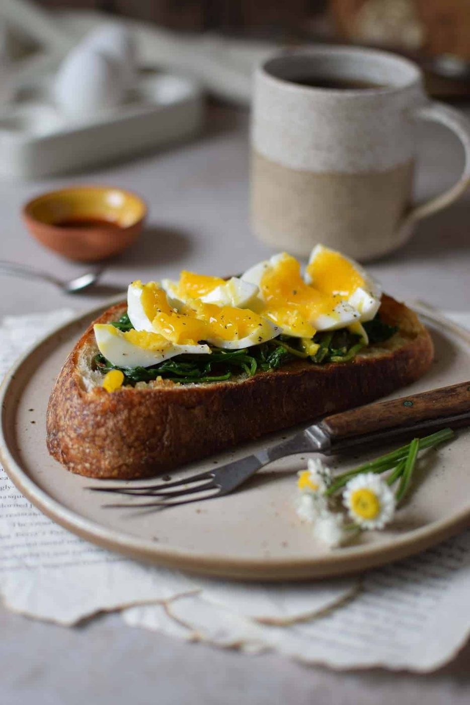 Smashed jammy eggs on toast with spinach on a brown plate.