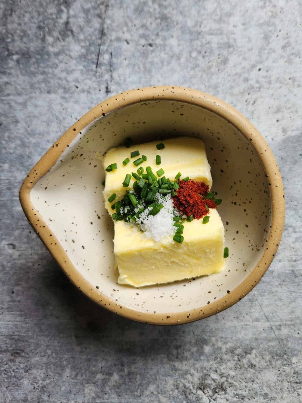 Butter, chives, and spices in a small beige bowl.