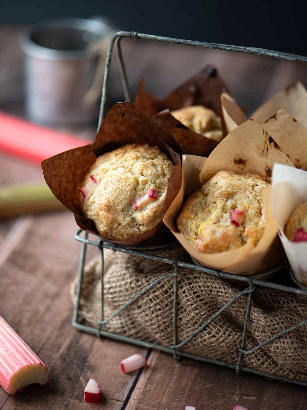 Rhubarb muffins in a metal basket with stalks of rhubarb to the side.