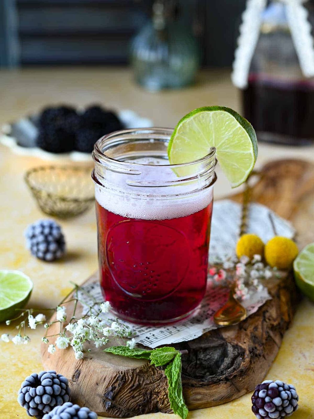 Blackberry soda in a clear glass with a lime wedge on a yellow surface.