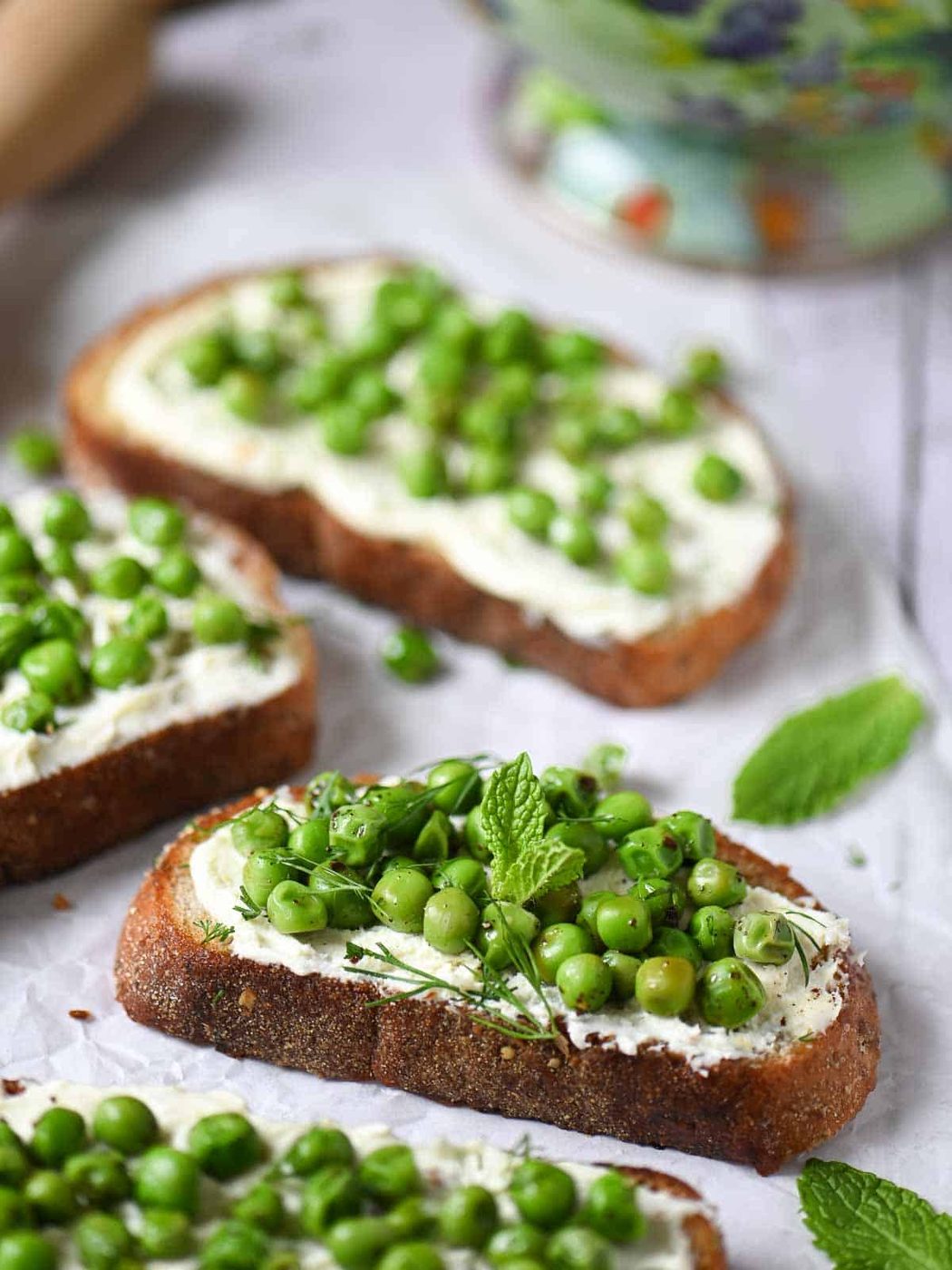 Pea toasts with mascarpone and fresh herbs on a white board.
