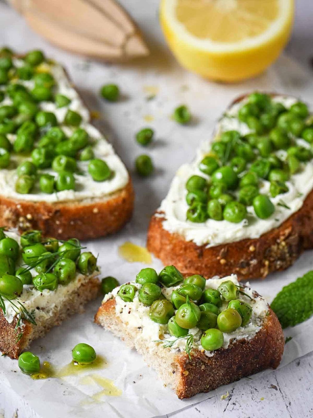 Pea toasts on a white board with lemon in the back.
