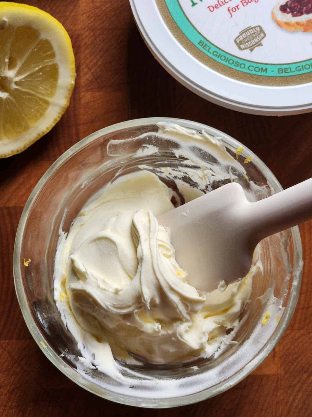 A white spatula in a clear bowl of mascarpone.