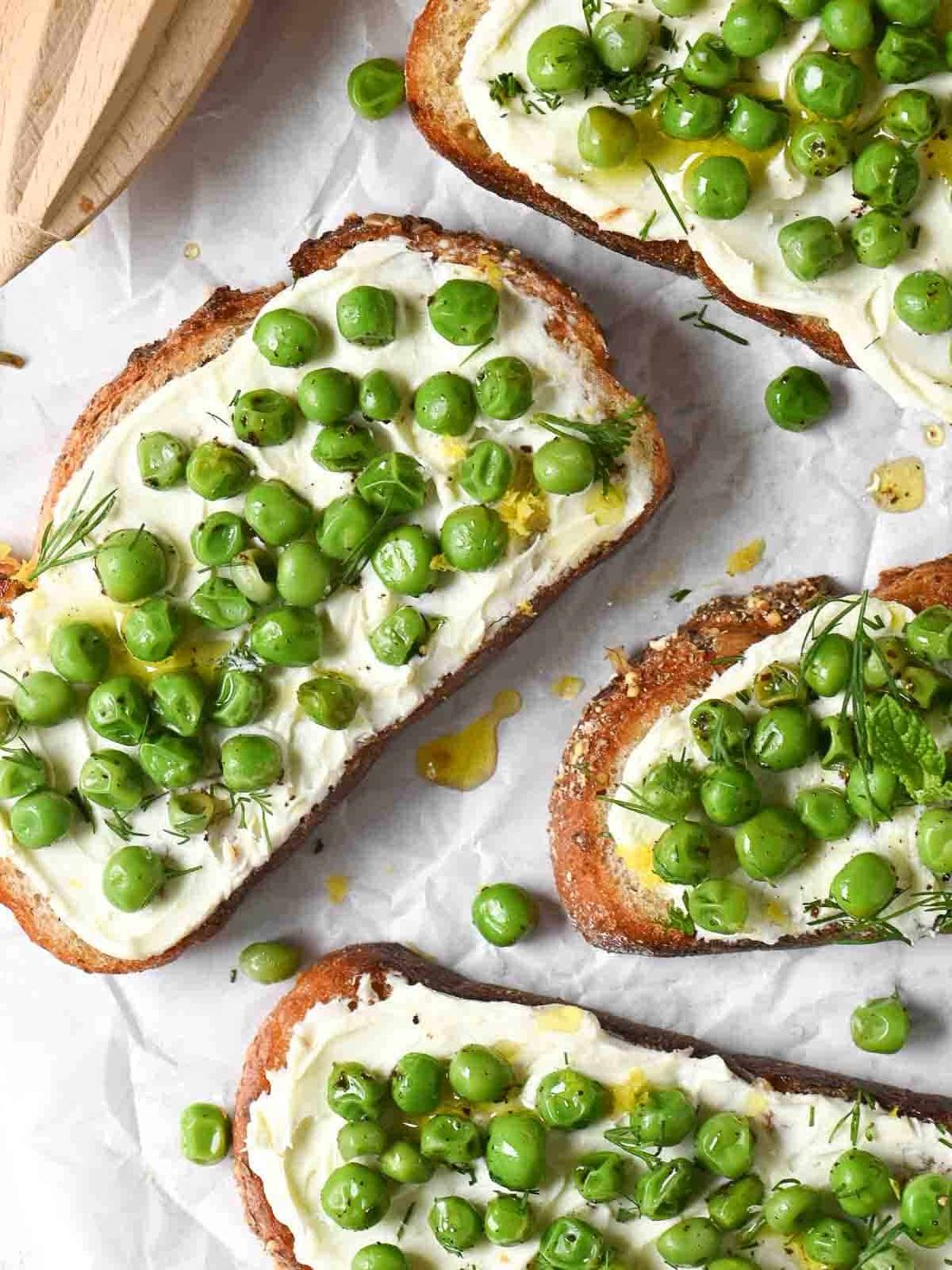Overhead of pea toasts with mascarpone on white parchment.
